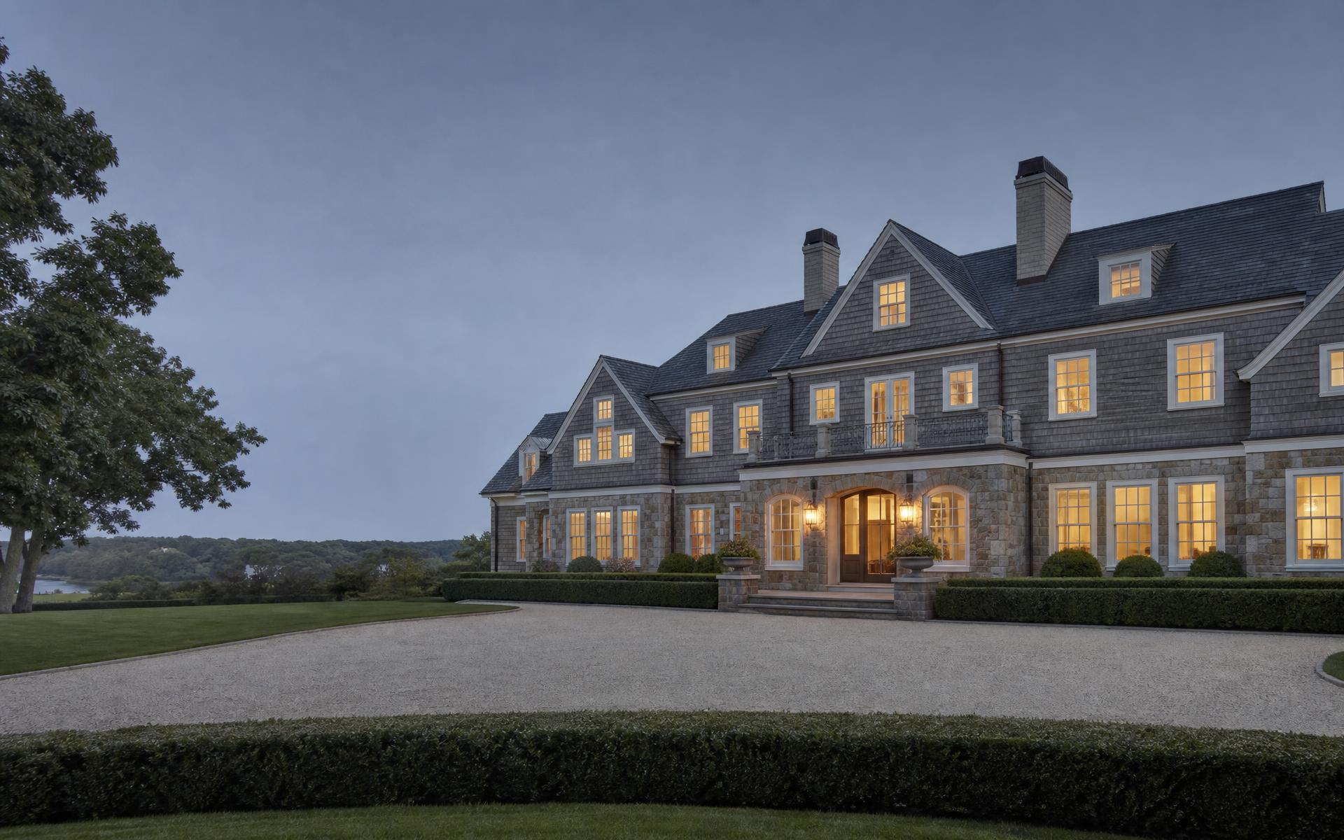 A stone and shingle New England estate at dusk with warm window light